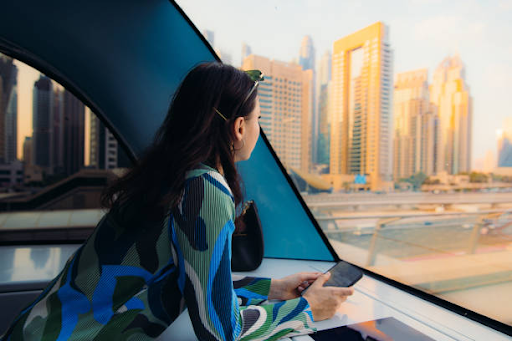 A woman looks out at Dubai's skyline while holding her phone, symbolizing steps to secure a residence visa in Dubai.